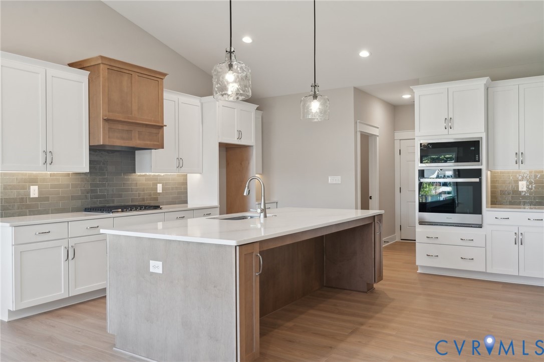 Kitchen featuring white shaker-style cabinetry, quartz countertops, a central island with a contrasting wood-tone base, integrated stainless steel double wall ovens, and a tile backsplash