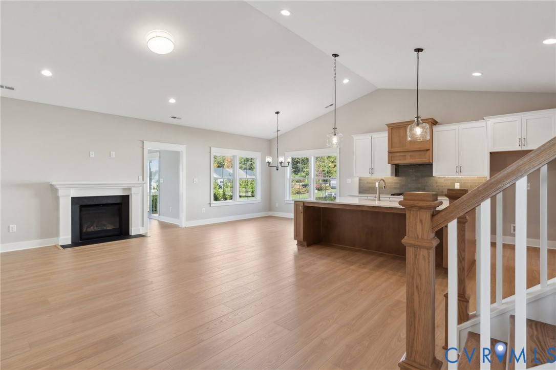 Vaulted ceilings, wood-finish flooring, fireplace with a white mantel, kitchen island with wood cabinetry, and recessed lighting