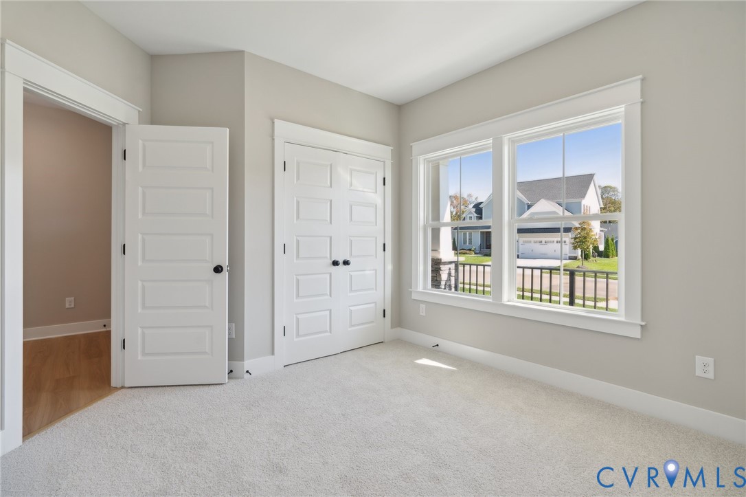 Neutral-toned interior featuring wall-to-wall carpeting, multi-pane windows with detailed casing, and white four-panel interior doors with matte black hardware