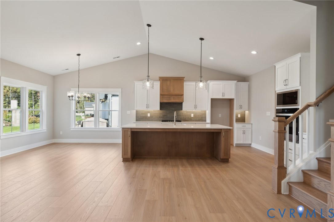 Kitchen featuring a vaulted ceiling, wood-finish flooring, two-tone cabinetry with an integrated vent hood, a center island with countertop seating, and built-in wall appliances