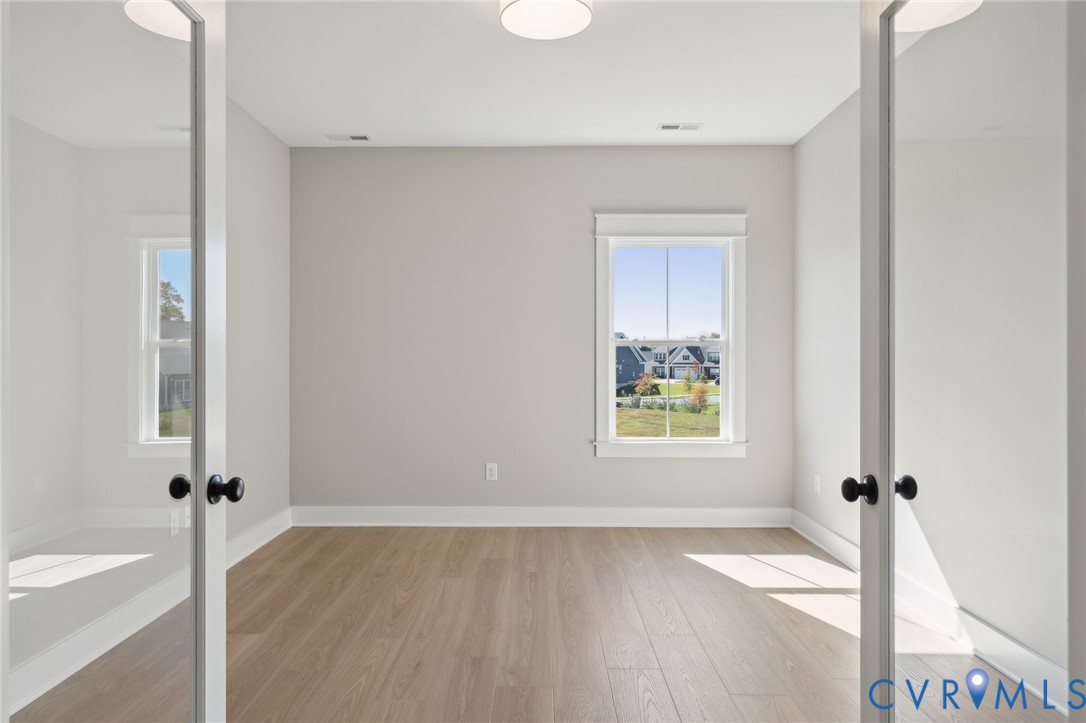 Room featuring wood-finish flooring, white French doors with matte black hardware, and a window with white casing