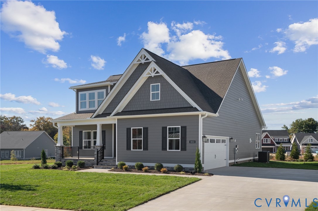 Two-story residence featuring grey lap siding, stone veneer accents, decorative gable truss detailing, a covered front porch with metal railing, and an attached two-car garage
