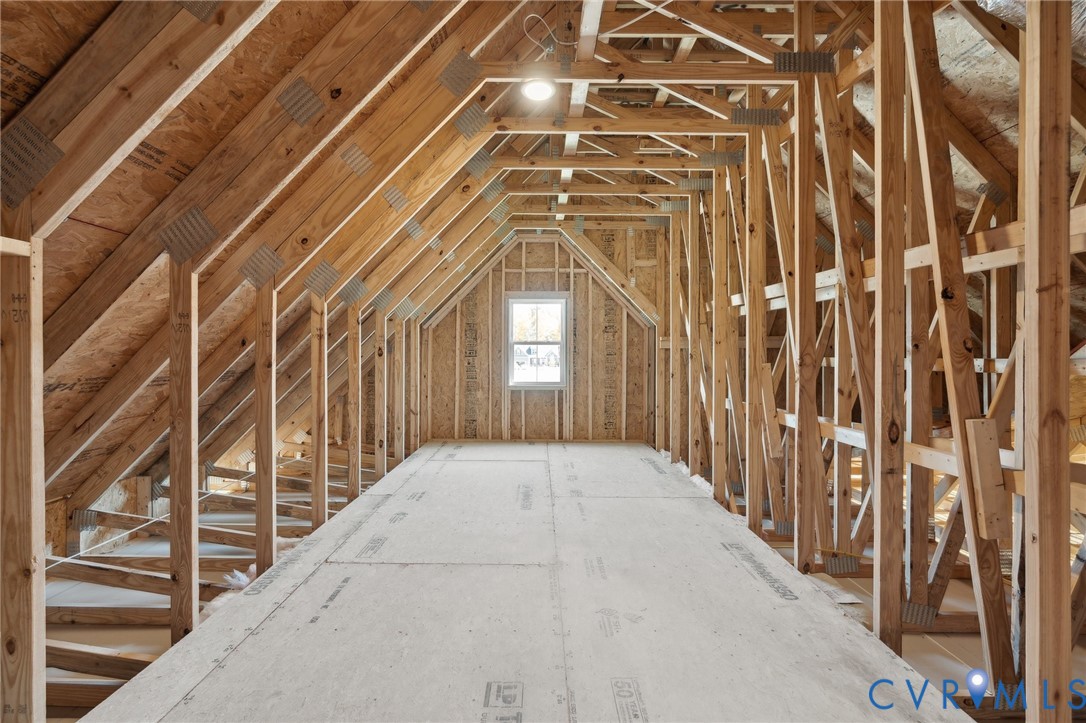 Unfinished attic space featuring exposed wood framing, gable truss construction, plywood subflooring, and a singular window
