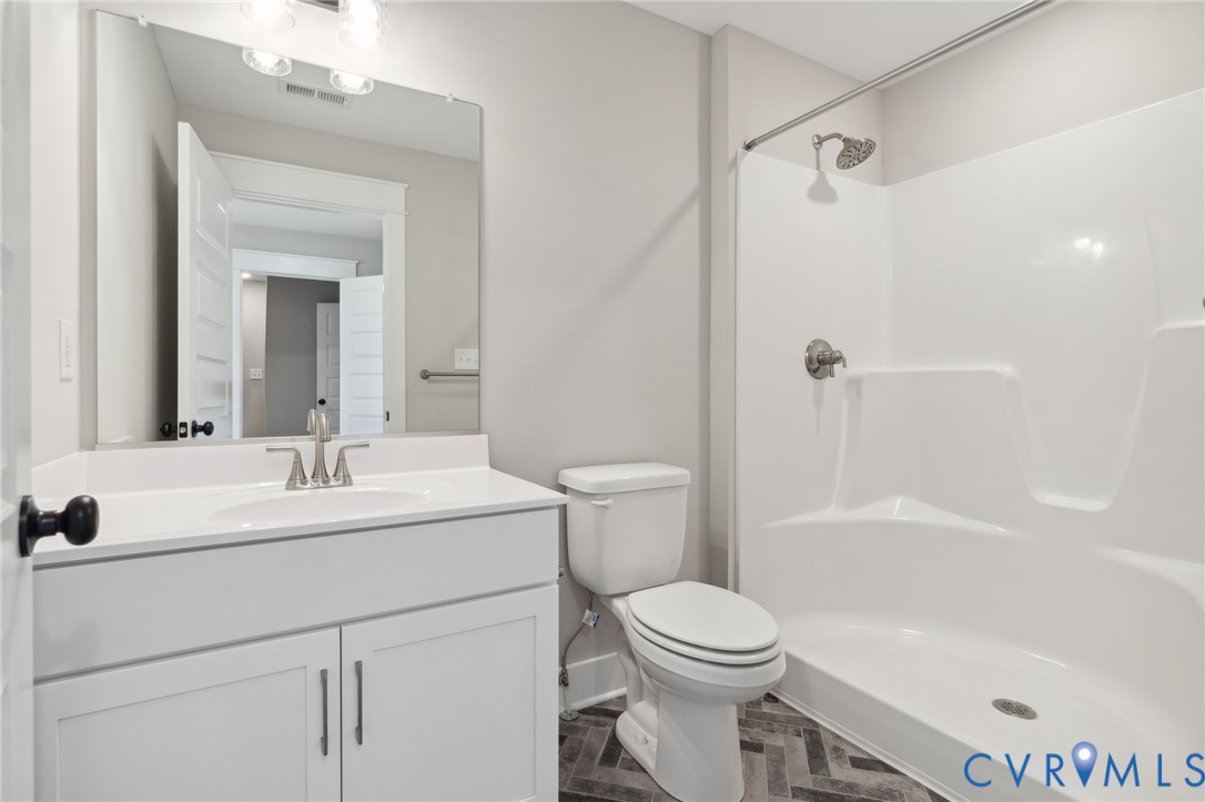 Bathroom featuring a white vanity cabinet with a stone countertop, integrated sink, oversized wall-mounted mirror, and a tub-shower combination with a surround, complemented by herringbone-pattern flooring