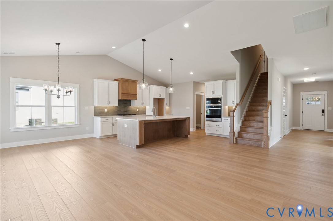 Vaulted ceiling, wood-finish flooring, kitchen island with cabinetry, built-in double wall oven, and wood-finish staircase