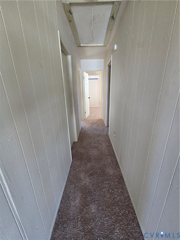 Hallway featuring vertical paneling, carpet flooring, and ceiling attic access Hallway featuring vertical paneling, carpet flooring, and ceiling attic access