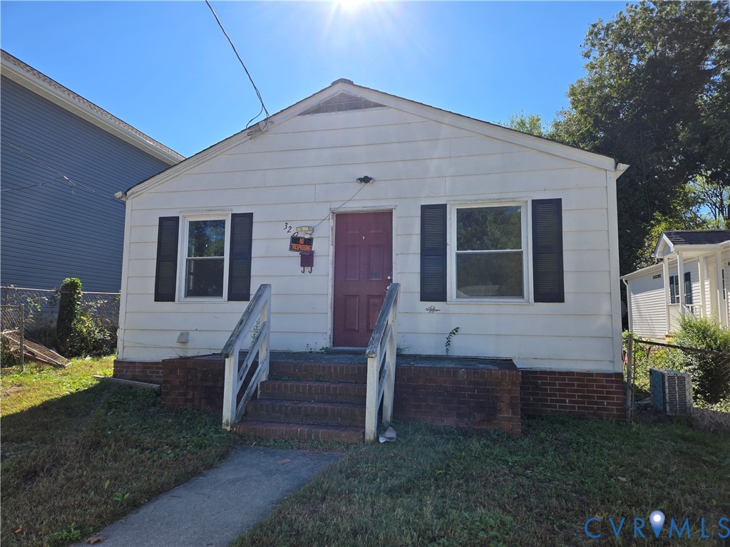Single-story exterior featuring white horizontal siding, dark decorative shutters, brick masonry foundation, and front steps with railings Single-story exterior featuring white horizontal siding, dark decorative shutters, brick masonry foundation, and front steps with railings