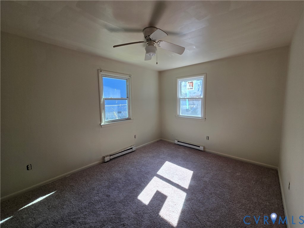Interior room featuring neutral-toned carpeting, two windows, and a ceiling-mounted fan with light fixture Interior room featuring neutral-toned carpeting, two windows, and a ceiling-mounted fan with light fixture