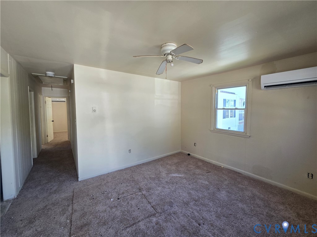 Room featuring neutral walls, carpeting, a ceiling fan, and a wall-mounted ductless heating and cooling unit Room featuring neutral walls, carpeting, a ceiling fan, and a wall-mounted ductless heating and cooling unit