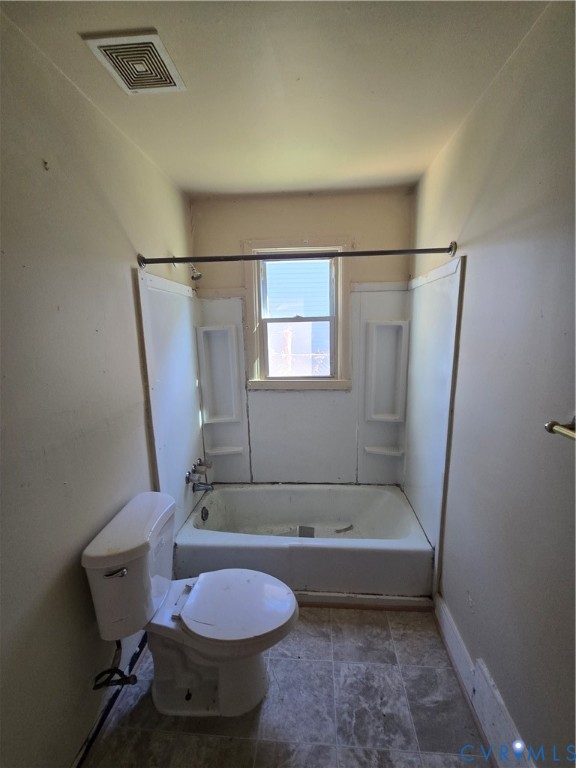 Bathroom featuring a white porcelain toilet, bathtub with integrated shelving, and tiled flooring Bathroom featuring a white porcelain toilet, bathtub with integrated shelving, and tiled flooring