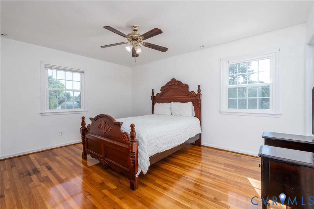 Room featuring wood-finish flooring, two double-hung windows with muntins, and a ceiling fan with integrated lighting