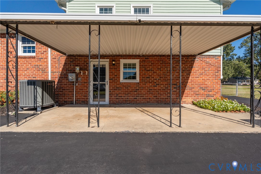 Covered carport featuring a concrete pad, decorative wrought iron supports, brick exterior cladding, and an asphalt driveway