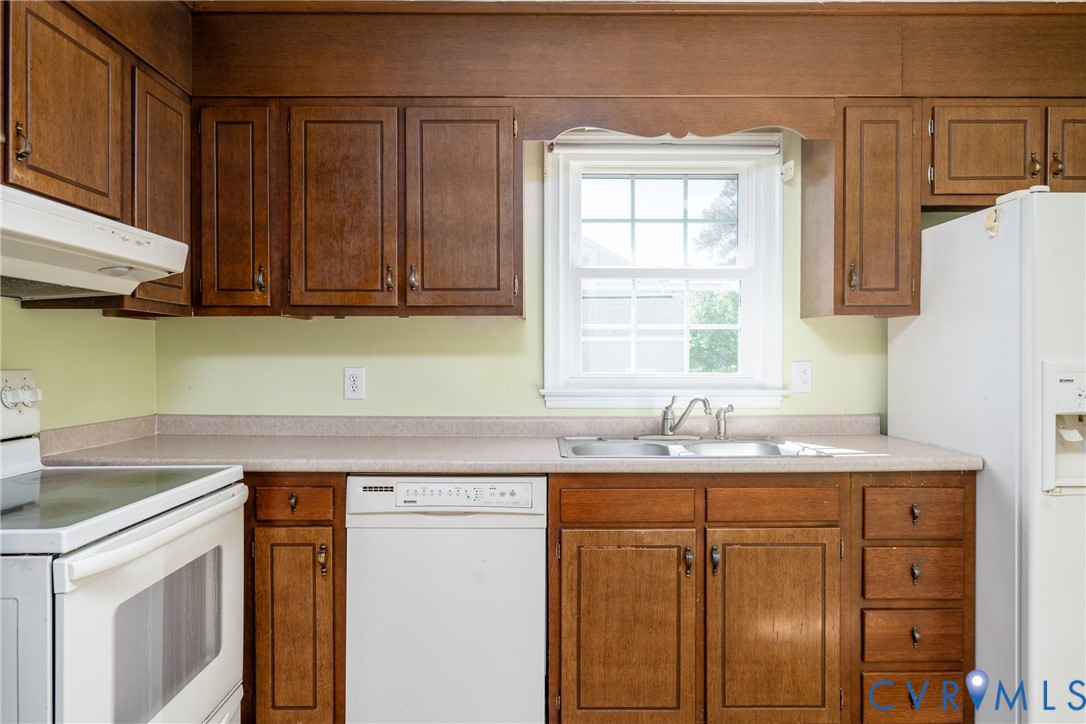Kitchen featuring wood cabinetry, integrated white appliances, a solid-surface countertop, and a double-basin stainless steel sink