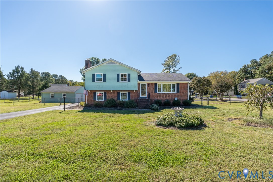 Split-level exterior featuring a brick and horizontal siding facade, multiple windows with shutters, an attached garage, and an expansive lawn Split-level exterior featuring a brick and horizontal siding facade, multiple windows with shutters, an attached garage, and an expansive lawn