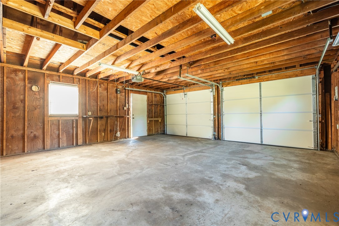 Two-car garage featuring exposed wood ceiling joists, concrete flooring, dual white sectional garage doors, and a dedicated entry door