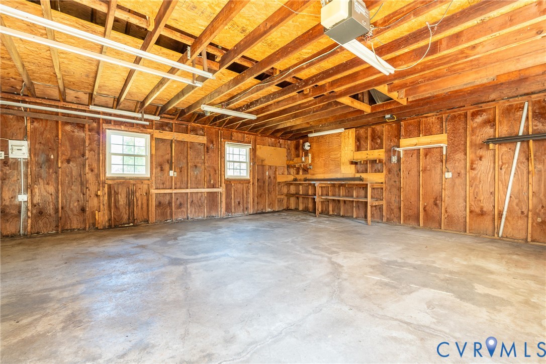 Garage space featuring exposed beam construction, concrete flooring, double-hung windows, and built-in shelving
