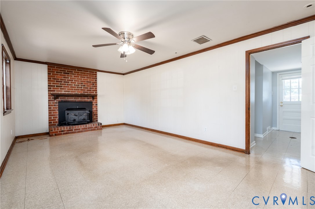 Brick fireplace with integrated stove insert, tile flooring, crown molding, and ceiling fan