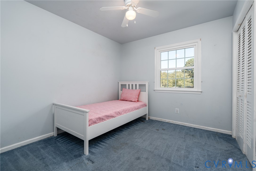 Room featuring wall-to-wall carpeting, a multi-pane window with trim, a white ceiling fan with integrated lighting, and a closet with louvered doors