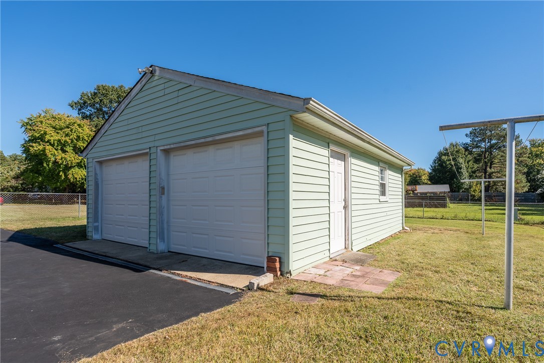 Detached two-car garage featuring light green horizontal siding, two white roll-up doors, and an asphalt driveway