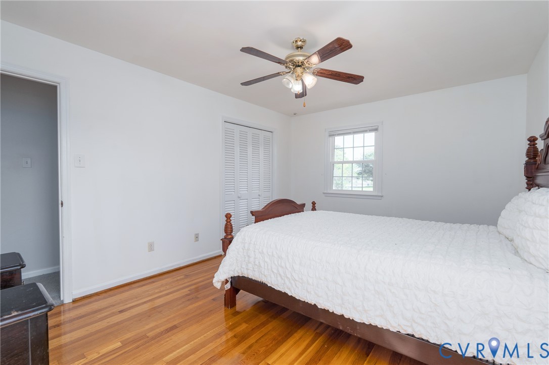 Room featuring wood-finish flooring, a ceiling fan with integrated lighting, a double-panel closet with louvered doors, and a multi-pane window