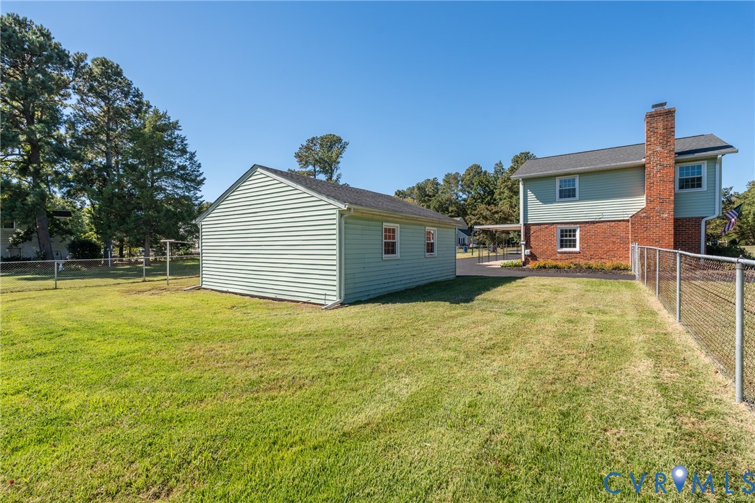 Exterior featuring a detached garage, brick and vinyl siding, an expansive grassy lot, and chain-link perimeter fencing