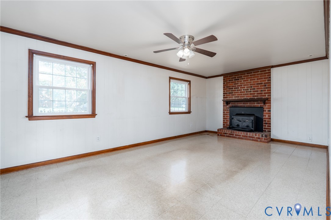 Brick fireplace featuring a wood-burning insert and mantel, large paneled windows with wood trim, and a ceiling fan with integrated lighting
