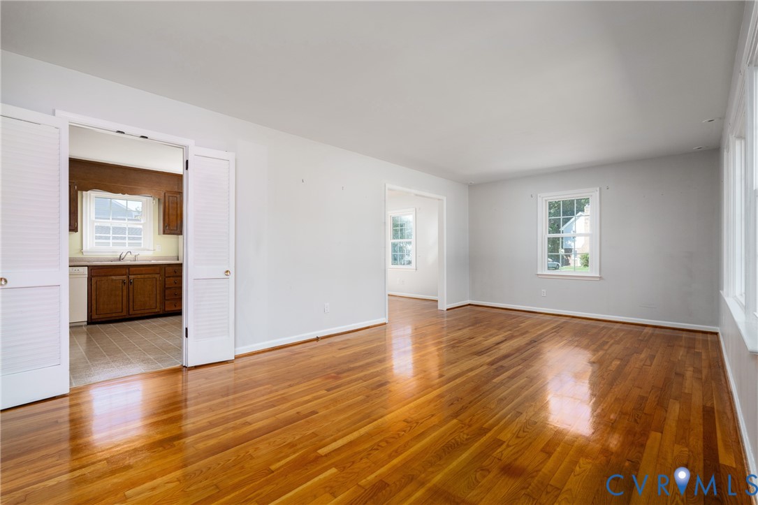 Interior space featuring polished wood-finish flooring, neutral wall paint, multi-pane windows, and white-paneled bi-fold doors Interior space featuring polished wood-finish flooring, neutral wall paint, multi-pane windows, and white-paneled bi-fold doors