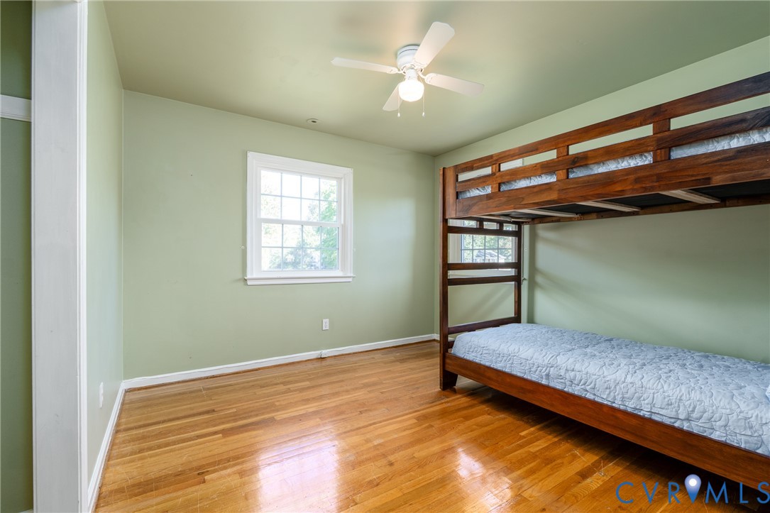 Room featuring wood-finish flooring, a multi-pane window, and a ceiling-mounted light fixture with a fan