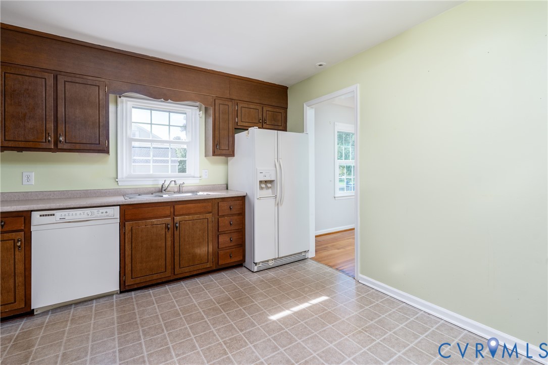 Kitchen featuring wood cabinetry, laminate countertops, a double-basin stainless steel sink, a dishwasher, and a refrigerator