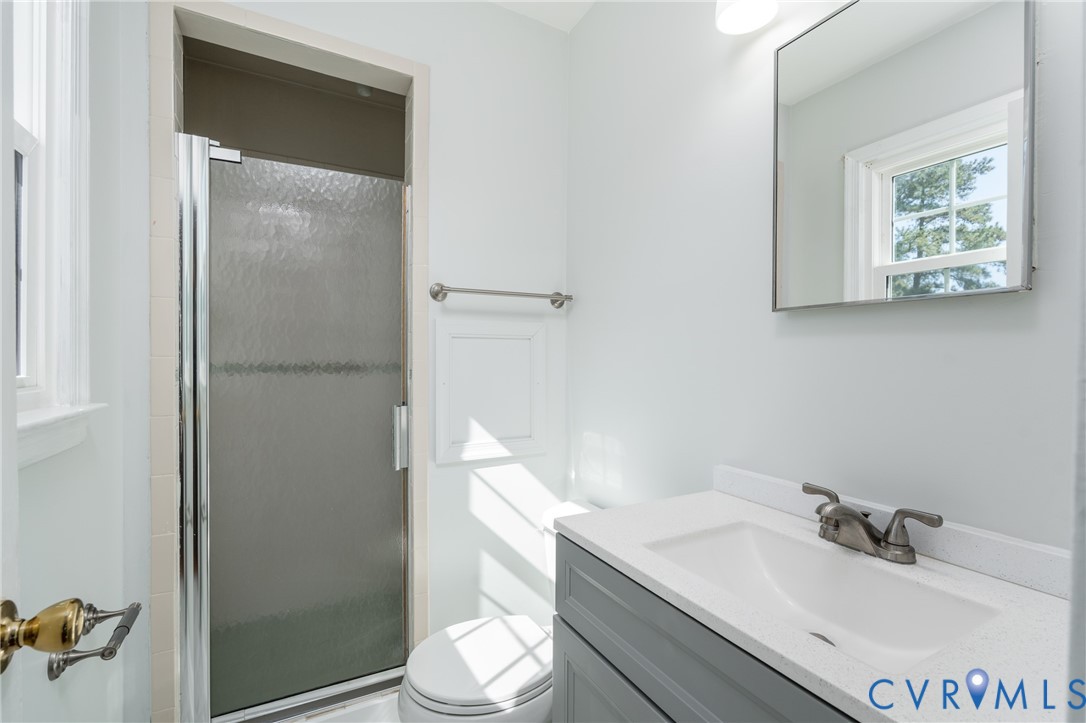 Bathroom featuring a gray vanity with a stone-composite countertop, integrated sink, chrome-finish faucet, and a shower enclosure with textured glass