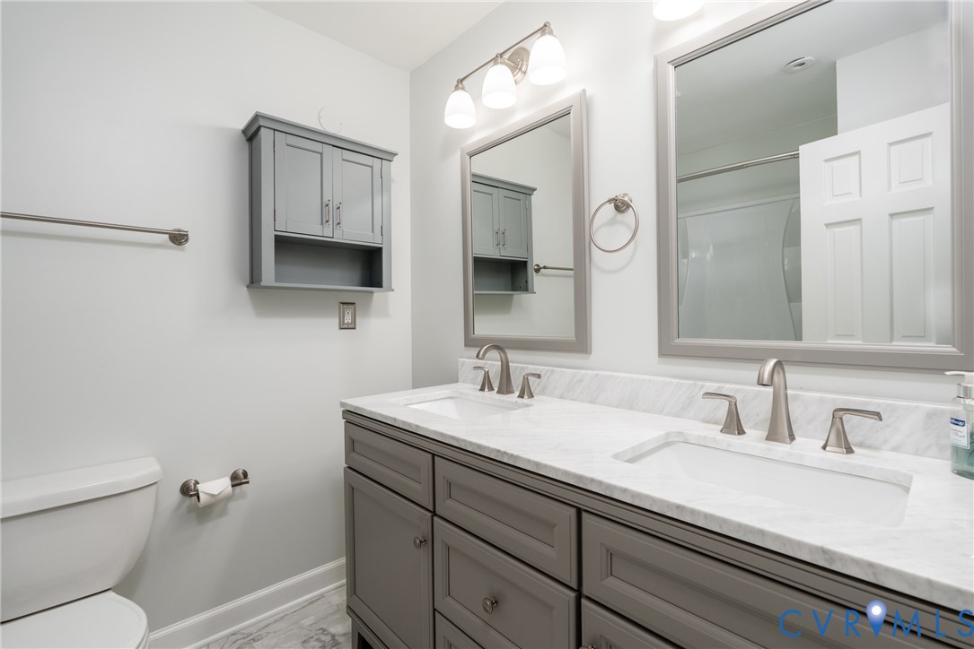 Double vanity featuring a light-toned countertop, under-mount sinks, brushed nickel faucets, grey cabinetry, and framed mirrors