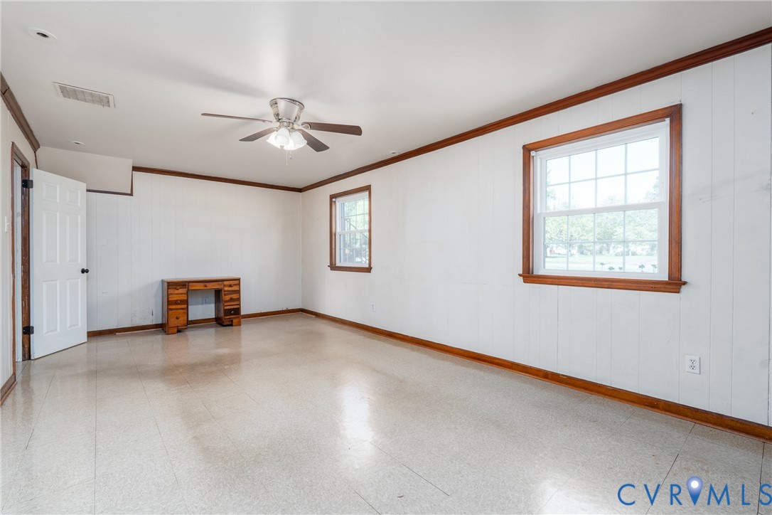 Room featuring white paneled walls, wood-finish trim, tile flooring, and a ceiling-mounted light fixture with a fan