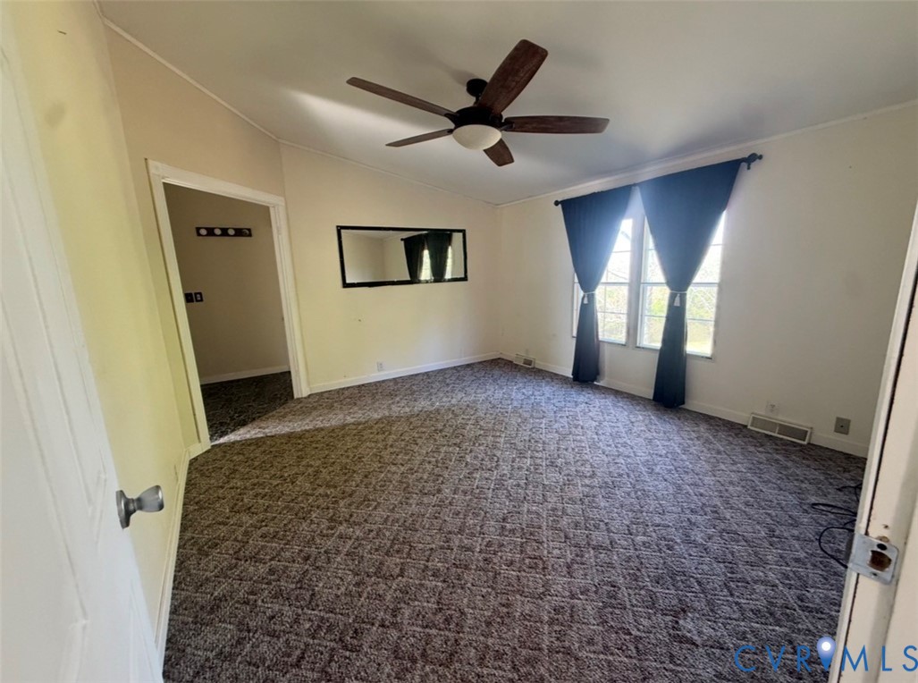 Spacious room featuring vaulted ceilings, a central multi-blade ceiling fan with integrated lighting, wall-to-wall patterned carpeting, and large dual windows