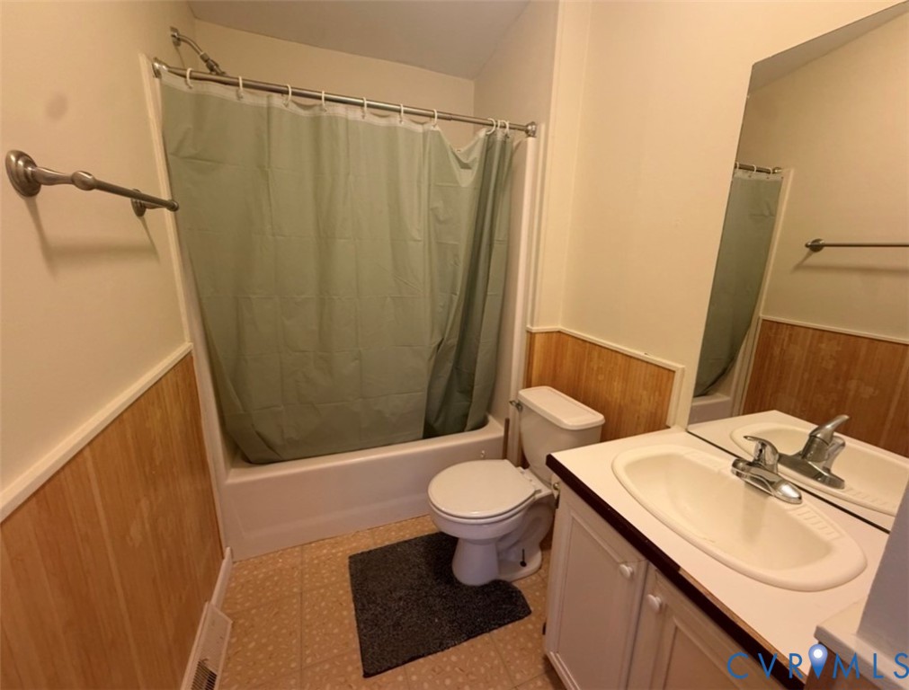 Bathroom featuring wood-paneled walls, vanity with integrated basin, chrome-finish plumbing fixtures, and a tub-shower combination