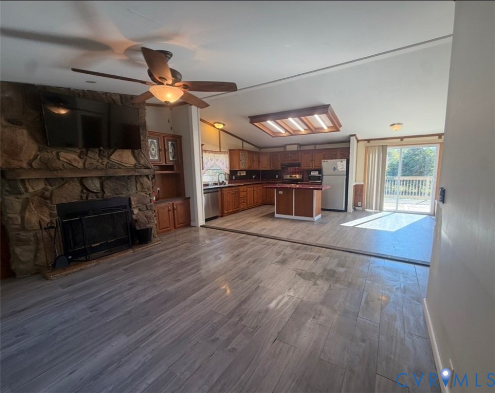 Stone-faced fireplace with hearth, wood-finish flooring, kitchen island, built-in cabinetry, and sliding glass doors