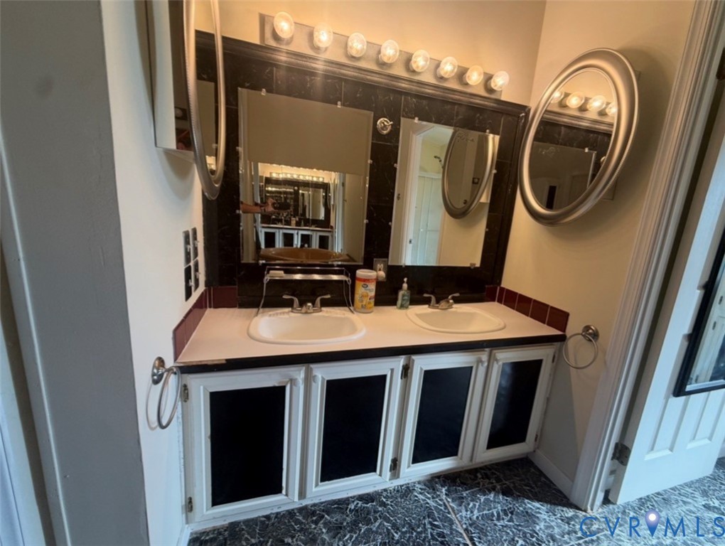 Dual-sink vanity featuring inset cabinetry with contrasting paneling, integrated mirrors, a polished countertop, and a multi-bulb vanity light fixture