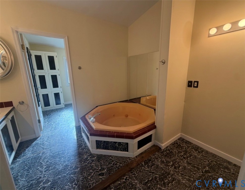 Octagonal soaking tub with tile surround, patterned flooring, wall-mounted mirror, and overhead vanity lighting