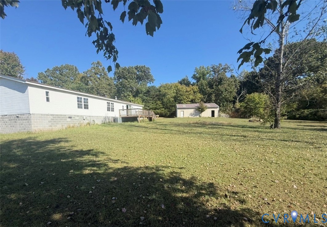 Expansive grounds featuring a wood deck, detached structure, concrete block foundation, and mature trees