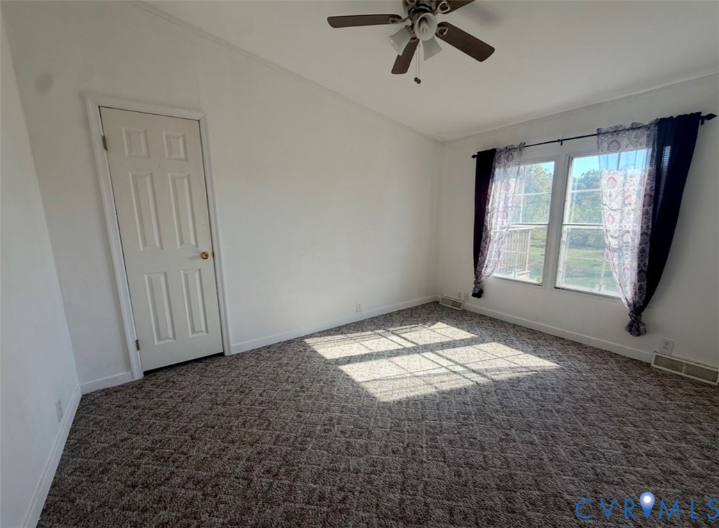 Vaulted ceiling room featuring neutral carpeting, a multi-blade ceiling fan with integrated lighting, and dual windows