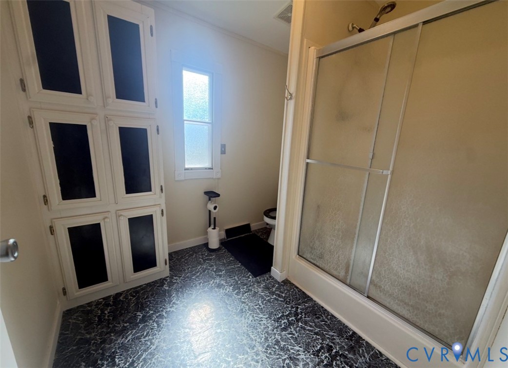 Built-in floor-to-ceiling cabinetry with multi-pane cabinet doors, walk-in shower with sliding glass enclosure, and patterned stone-finish flooring