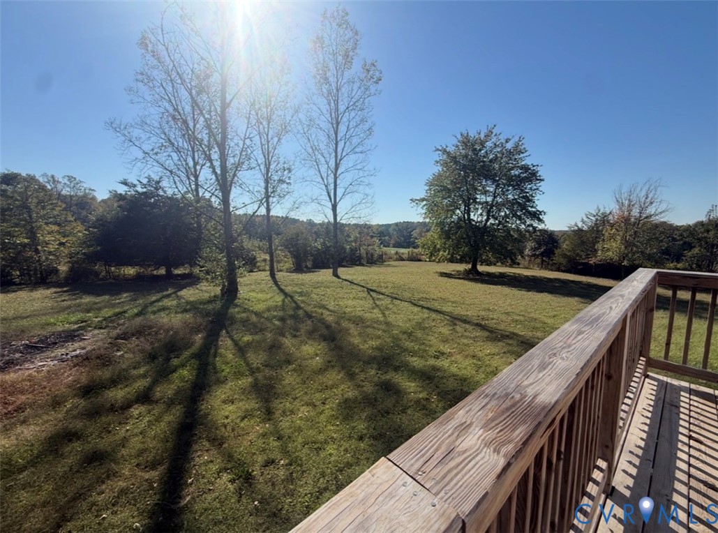 Elevated wooden deck featuring vertical balusters overlooking an expansive lawn with mature trees and native landscape
