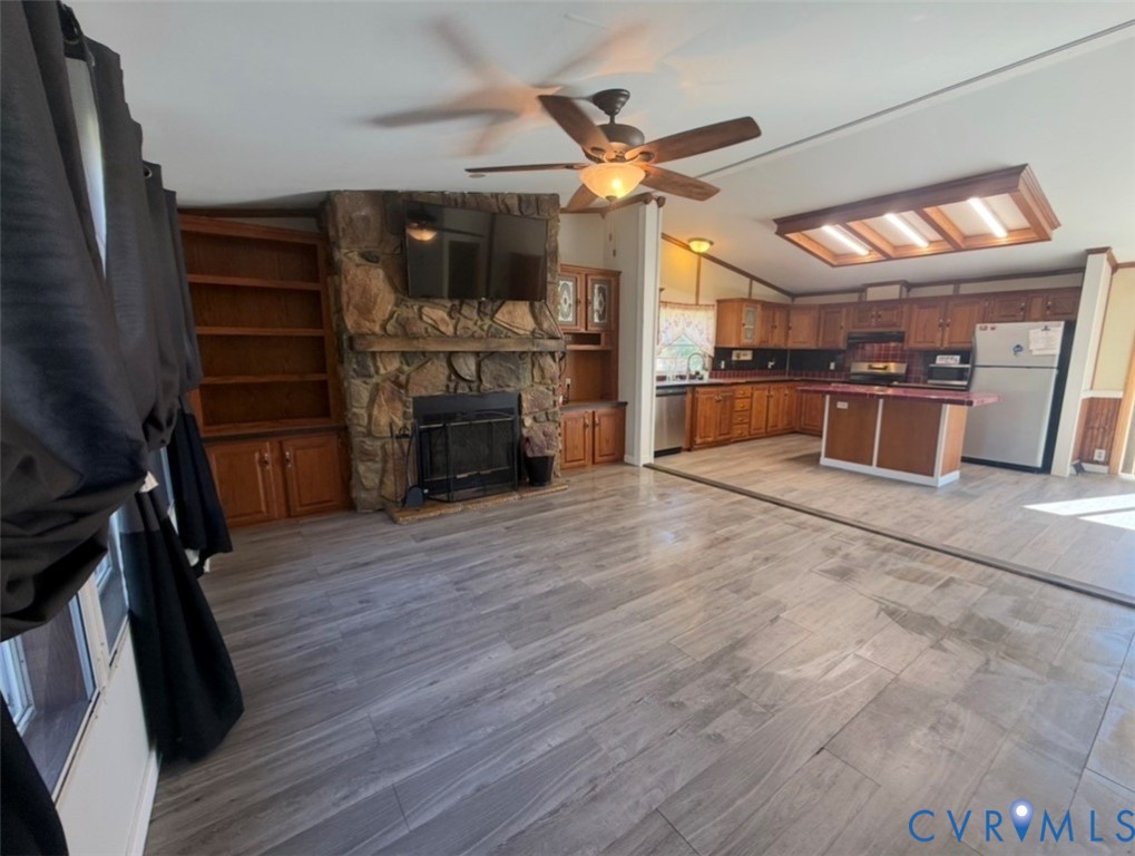 Floor-to-ceiling stone fireplace with built-in cabinetry, wood-finish flooring, central island, and wood cabinetry