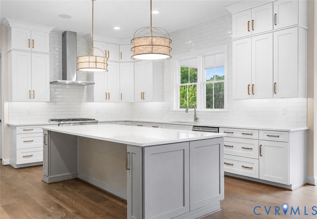 Kitchen featuring white shaker-style cabinetry, quartz countertops, a central island with a grey finish, white subway tile backsplash, and wood-finish flooring Kitchen featuring white shaker-style cabinetry, quartz countertops, a central island with a grey finish, white subway tile backsplash, and wood-finish flooring