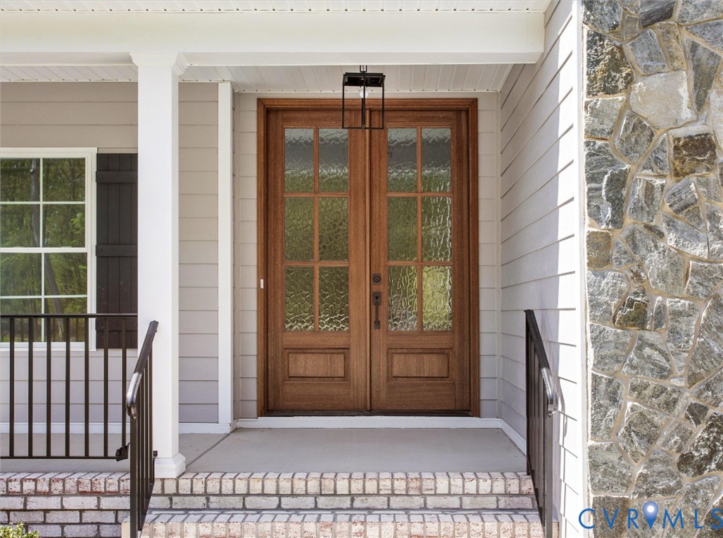 Double front entry doors with wood finish and seeded glass panes, stone veneer facade, brick-trimmed porch steps, and metal railing