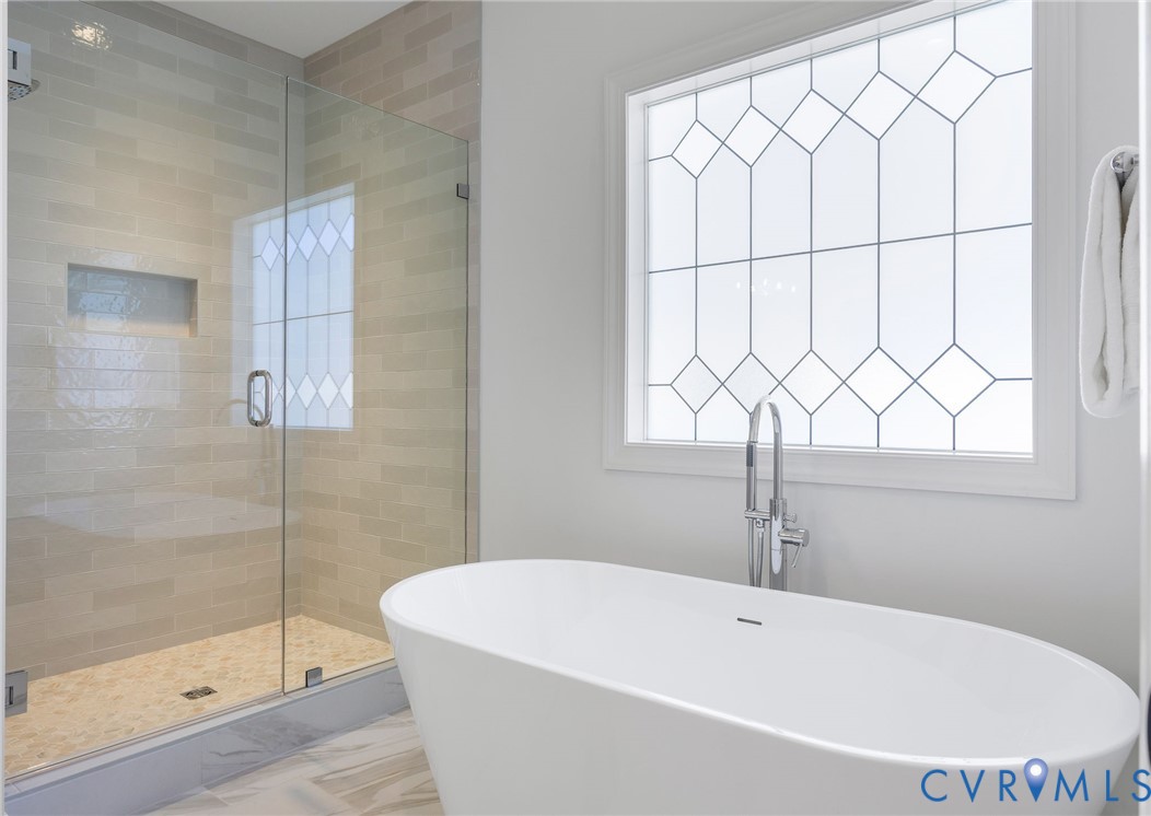 Freestanding soaking tub with a floor-mounted faucet, glass-enclosed shower featuring a recessed wall niche, and decorative window glass
