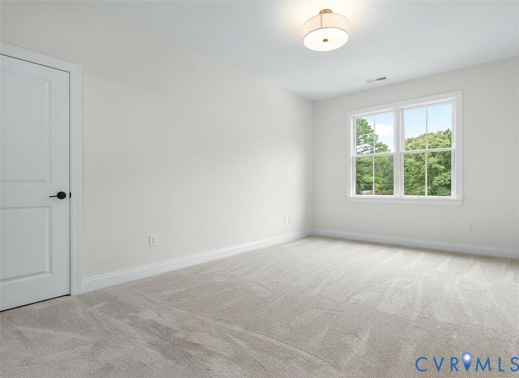 Neutral-toned carpeting, double-hung windows, flush-mount drum lighting, and a paneled interior door with matte black hardware