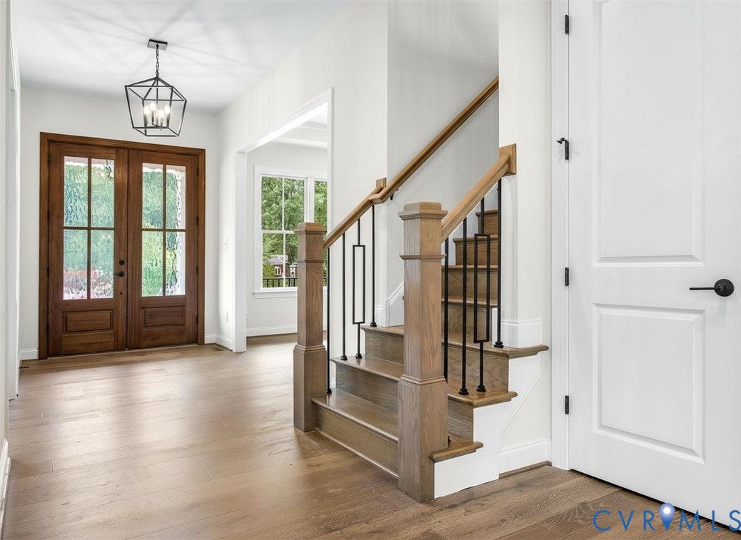 Entryway featuring double wood-paneled doors, wood-finish flooring, a geometric metal pendant light, and a staircase with wood handrails and black metal balusters