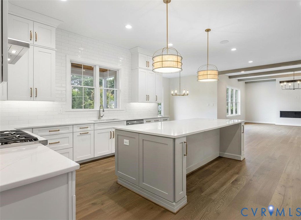 Kitchen featuring white shaker-style cabinetry, a quartz-topped center island, white subway tile backsplash, drum pendant lighting, and wood-finish flooring