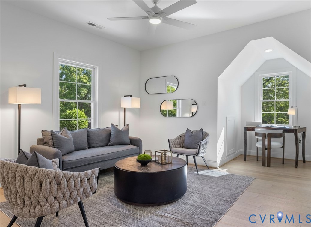Light-filled room featuring wood-finish flooring, a white ceiling fan with integrated lighting, multipane windows, and a recessed dormer area