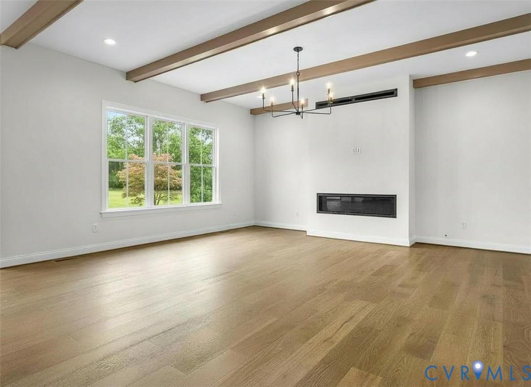 Living area featuring wood-finish flooring, exposed ceiling beams, a linear wall-mounted fireplace, and a multi-arm chandelier